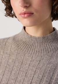 Beige ribsafe sweater with a high, textured collar. Soft wool material features vertical stripes and a fitted design.