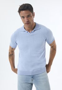 Camisa polo de manga corta azul claro con cuello plano, puños acanalados y tejido texturizado; combinada con jeans de mezclilla azul claro.