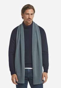 Grå strikket tørklæde med ribbede ender, båret over en marineblå sweater. Blød tekstur og rektangulær form, designet til varme og stil.