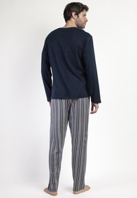 Camiseta de manga larga azul marino combinada con pantalones de pijama a rayas grises con patrones verticales en tonos beige y marrón. Material suave y corte relajado.