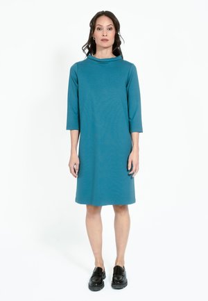 Teal värvi põlvikute pikkusega kleit, millel on kolmveerandi varrukad, kaelaauk ja vaba lõige. Kanda mustade platvormkingadega. Sile, pehme kangas.