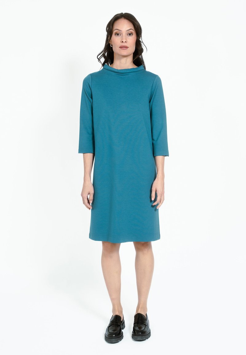 Teal knälång klänning med trekvartsärmar, en cowl-hals och en avslappnad passform. Bärs med svarta platåskor. Slätt, mjukt tyg.