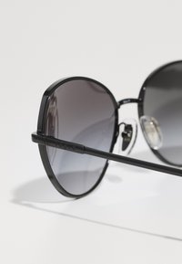 Óculos de sol oversized pretos com lentes de degradê, apresentando uma estrutura metálica elegante, dobradiças proeminentes e um logotipo discreto na haste.