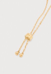 Złoty stalowy naszyjnik z centralnym ogniwem i podwójnymi łańcuszkami, kończącymi się dwiema kulkami akcentującymi. Gładka tekstura z polerowanym wykończeniem.