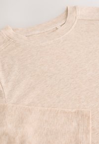 Beżowa prążkowana koszulka z długim rękawem, okrągłym dekoltem i widocznymi detalami przeszyć, charakteryzująca się miękką teksturą i luźnym krojem.