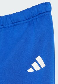Pantalons de survêtement en coton bleu avec une taille élastique et un logo Adidas blanc avec trois rayures diagonales sur le bas à gauche.
