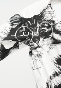 Ασπρόμαυρη εικονογράφηση μιας γάτας που φοράει στρογγυλά γυαλιά, τυπωμένη σε λευκό ύφασμα.