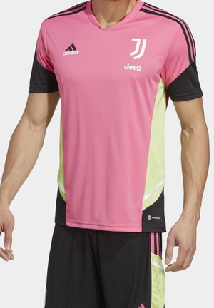 Homme portant un maillot de football Adidas Juventus rose et noir avec le logo Jeep et un short noir assorti avec des accents roses et jaunes.