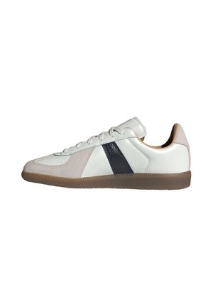 Sneaker bianca bassa con dettagli in suede beige, striscia laterale nera, lacci bianchi e suola in gomma marrone, mostrata di lato.