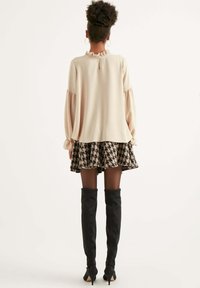 Krémový top s dlouhými rukávy a volánkovým výstřihem, doplněný o sukni s houndstooth vzorem v černé a krémové barvě. Černé vyšší kozačky dotvářejí celkový vzhled.