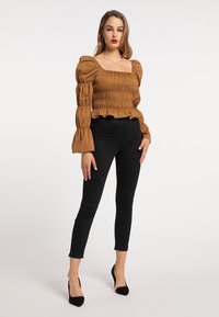 Atasan smocked cokelat dengan leher kotak, lengan bengkak, dan hem berenda. Dipadukan dengan celana jeans skinny hitam dan sepatu hak runcing hitam.