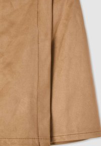 Tessuto scamosciato color cammello con una texture morbida, che mostra un dettaglio di cucitura, piegato in modo drappeggiato. Nessun motivo o elemento hardware visibile.