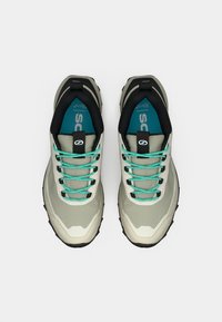 Lys grå treningssko med svarte detaljer, turkise lisser og teksturerte såler. Har en polstret innvendig del og forsterket hæl.