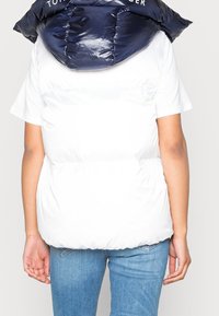 Biały pikowany kamizelka z granatowym kapturem, o gładkiej fakturze i kontrastujących kolorach. Na kapturze znajduje się logo "TOMMY HILFIGER".