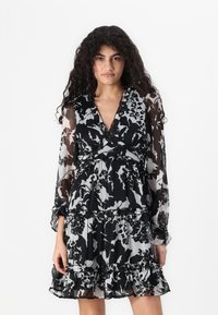 Haljina s crno-bijelim cvjetnim uzorkom, s volanima na rubu, dugim prozirnim rukavima i preklopljenim dekolteom, od laganog materijala.