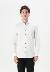 Chemise blanche à manches longues avec un col pointu et des boutons noirs sur le devant, présentant un léger éclat et des détails de poignets contrastés.