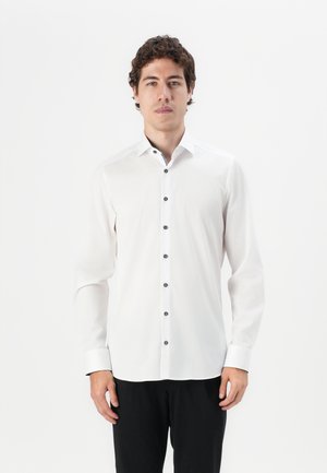 White long-sleeve shirt with a pointed collar and black buttons down the front, featuring a subtle sheen and contrasting cuff detail.