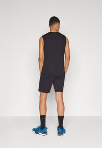Top atlético sin mangas negro con pantalones cortos a juego, con un ajuste relajado. Combinado con zapatillas azules y calcetines negros. Diseño simple.