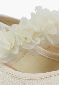 Bailarinas en tela rosa empolvado con un delicado acento de flor de malla blanca en la correa, con una textura suave y un diseño sencillo.
