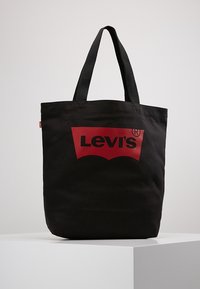 Sac en toile noir avec un logo Levi's rouge bien en vue et de courtes anses noires robustes. Design simple et pratique.