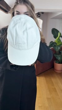 White cotton baseball cap with curved brim and embroidered logo on the front. Smooth texture, worn by a person holding it forward.