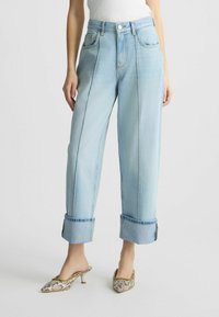 Blugi largi de culoare albastru deschis, din denim, având manșete răsucite și sistem de închidere prin buton frontal, cu două buzunare laterale și detalii cu cusături.