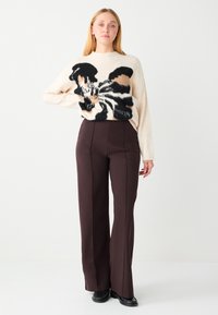 Crèmesweater met zwart-bruine abstracte print, gecombineerd met hooggetailleerde donkerbruine brede broekspijpen en zwarte schoenen.