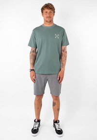 T-shirt gris à manches courtes avec un petit motif imprimé, associé à un short gris clair et des baskets montantes noires avec des lacets blancs.