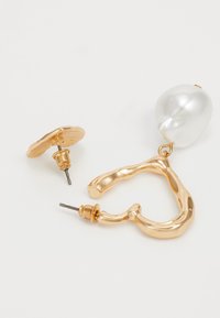 Pendientes en tono dorado que presentan una forma abstracta texturizada y un gran acento de perla blanca lisa. Incluyen un componente de respaldo redondo.