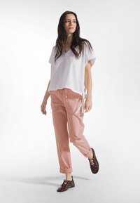 Biały bawełniany top z dekoltem w serek, luźny krój; różowe bawełniane spodnie z podwiniętymi nogawkami; ciemnobrązowe sznurowane buty z zaostrzonym noskiem. Neutralne tło.