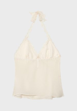 Kremna halterneck majica s čipkastim robom in prozornim materialom, zavezana z lokom na vratu.