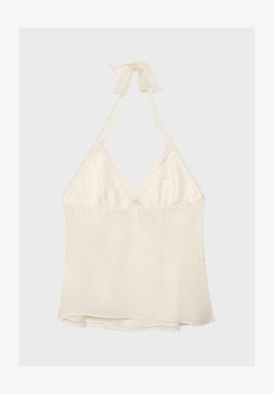 Kremna halterneck majica s čipkastim robom in prozornim materialom, zavezana z lokom na vratu.