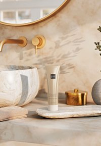 Detox shampoo in a sleek, gold and white tube with embossed logo, placed on a light stone tray next to a marble bowl and golden canister.