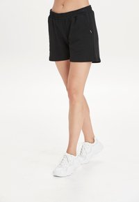 Svart bomullsshorts med elastisk midja, med sidofickor och en avslappnad passform. Kombinerat med vita snörskor.