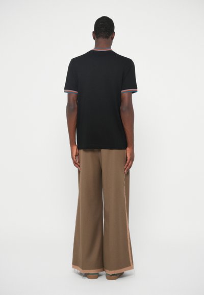 Melna īsām piedurknēm T-krekls ar daudzkrāsainu ribota tipa apkakli, saskaņots ar platām brūnām biksēm ar kontrastējošu sānu svītru.