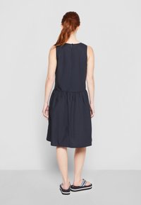 Vestido sin mangas de color azul marino con cintura fruncida, falda de longitud hasta la rodilla y cierre de ojal en la parte posterior. Tejido suave, diseño casual.