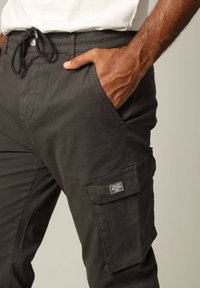 Donker cargo broek met een elastische tailleband en trekkoord. Heeft zijzakken en een patzak met logo-details. Gemaakt van een katoenmix.