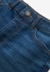 Jeans in denim blu scuro con cuciture arancioni, dotati di chiusura con bottone metallico e tasche frontali, che mostrano una trama liscia e un design informale.