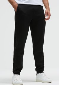 Schwarze Jogginghose mit slim fit, seitlichen Taschen, dezentem Branding in Schwarz an der Seite und gerippten Knöchelbündchen.