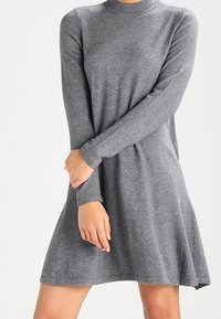 Robe grise à manches longues en tissu doux, mettant en avant une taille cintrée et une jupe évasée, avec un col haut.