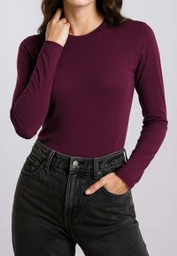 Top aderente a maniche lunghe in tessuto bordeaux intenso, abbinato a jeans neri a vita alta con tasca frontale e passanti per cintura.