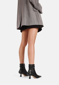 Stivali ankle neri con punta affusolata, realizzati in pelle liscia, dotati di tacco affusolato e cinturino decorativo alla caviglia con fibbia in metallo.