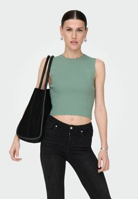 Zielony prążkowany crop top, czarne dżinsy z wysokim stanem oraz czarna zamszowa torebka na ramię z dwoma paskami. Gładka tekstura, dopasowany krój i minimalistyczne akcenty.
