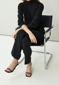 Svart stickad polotröja med åtsittande ärmar, tillsammans med svarta vida byxor och svarta remsandaler med klack. Kromstol med en minimalistisk design.