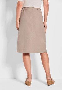 Beige Leinenrock mit einem Reißverschluss hinten, in Midi-Länge und mit einem sauberen Saum. Kombiniert mit beigefarbenen Keilsandalen mit einem strukturierten Korkabsatz.