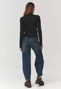 Czarny top z długim rękawem, dopasowany w talii, w połączeniu z szerokimi niebieskimi dżinsami. Dżinsy mają klasyczny krój pięciu kieszeni oraz wyblakłe wykończenie.