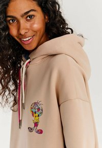 Béžová mikina vyrobená z mäkkej tkaniny, s farebnou grafikou kresleného charakteru na prednej strane a kontrastnými ružovými šnúrkami.