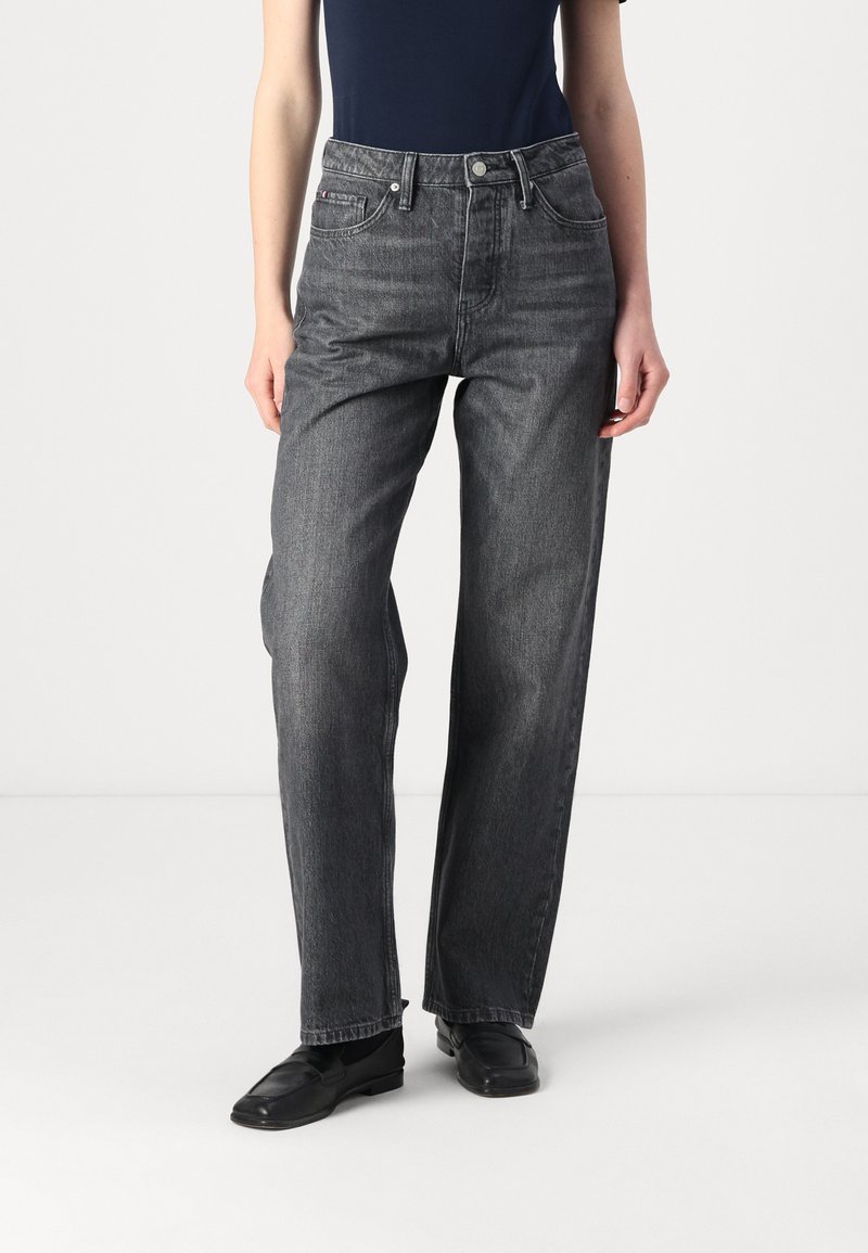 Jean taille haute, coupe droite en denim gris foncé. Comprend un design traditionnel à cinq poches et un léger délavage, assorti à des chaussures noires.