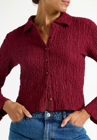 Sammenkrøllet burgunder knap-upp skjorte med krave, tekstureret stof, lange ærmer og en figursyet silhuet, parret med denimjeans.