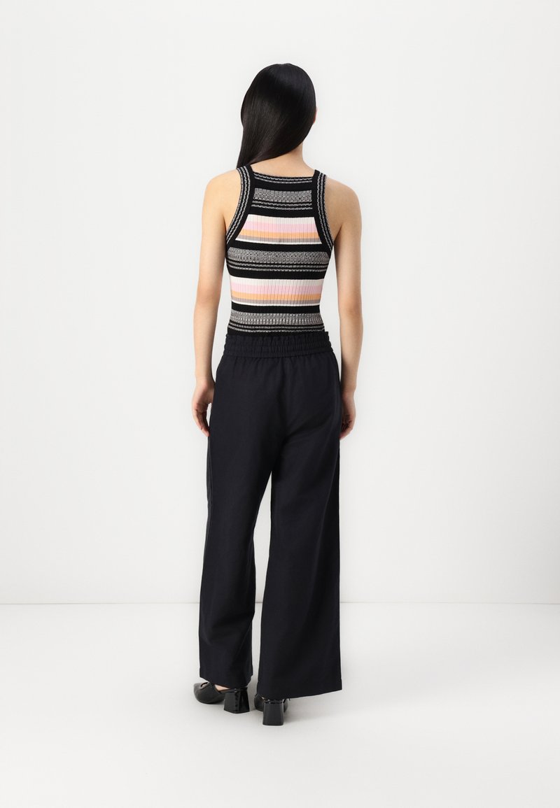 Mehrfarbiges, geripptes Tanktop mit dünnen Trägern, das horizontale Streifen in Pink, Schwarz und Grau aufweist. Kombiniert mit weiten schwarzen Hosen.